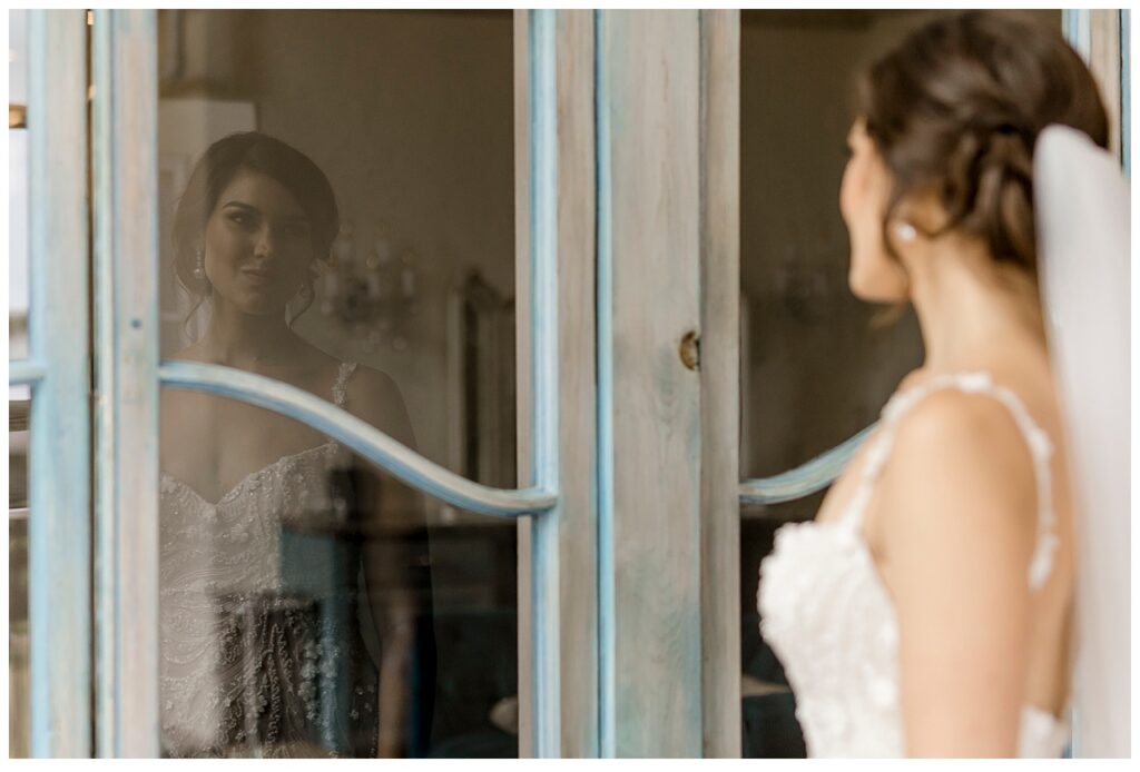 Bride looks at her reflection in the windows of a door at Bavaria Downs. 