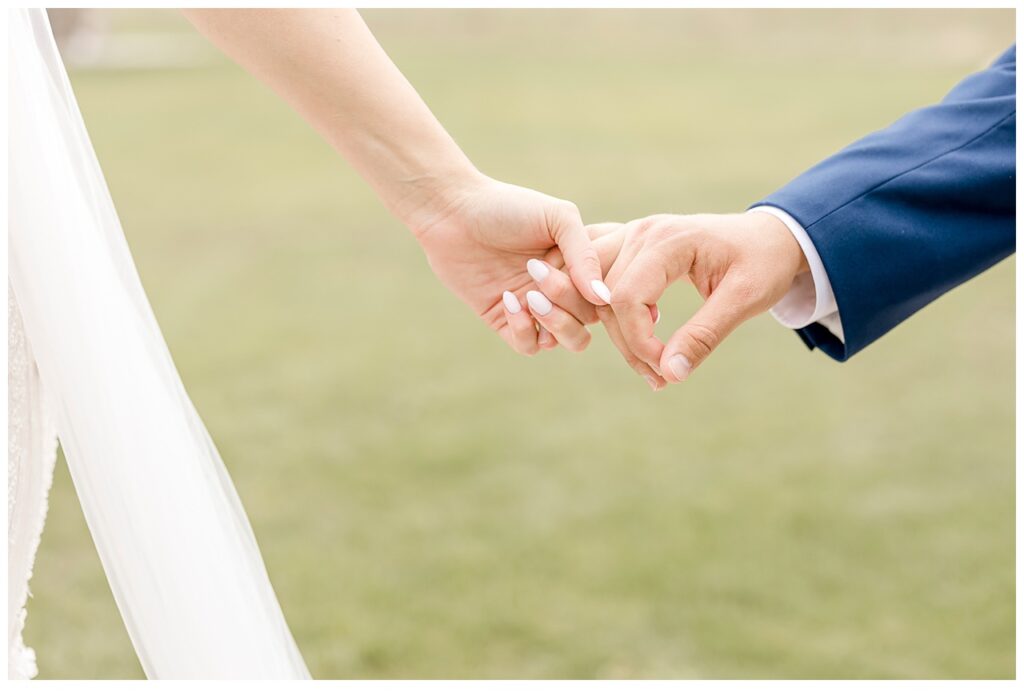 Closeup of newlyweds holding hands in a field on the grounds of Bavaria Downs in Chaska, MN. 