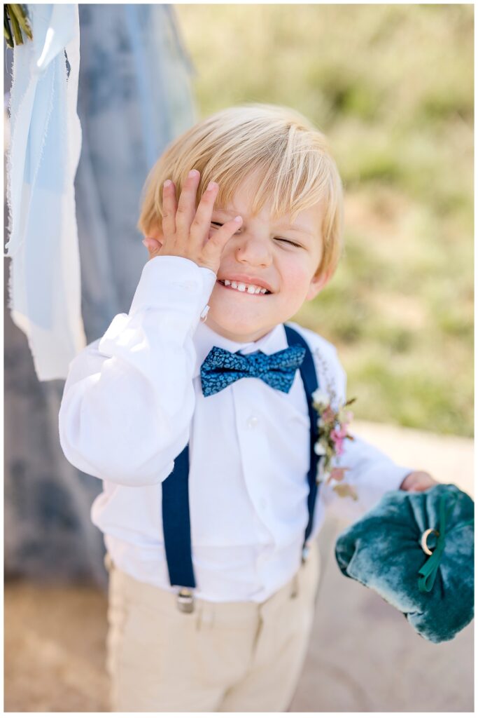 Small boy smiles with a hand on his face before he performs his ring bearer duties. 