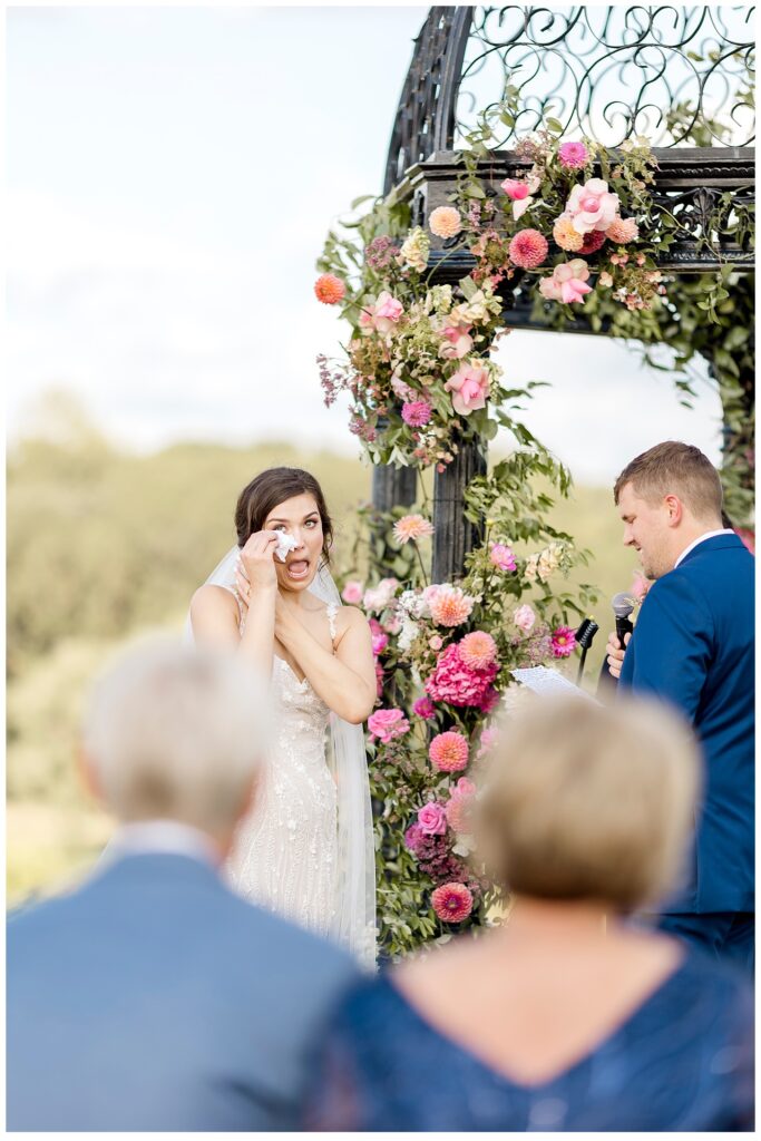 Bride wipes tears from her eyes as groom reads his vows during Bavaria Downs wedding ceremony. 