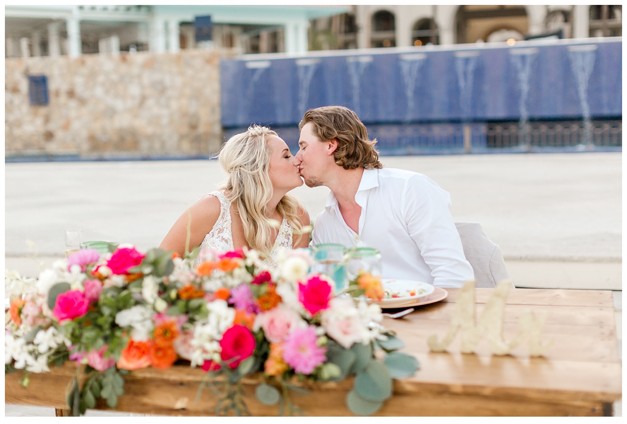 Newlyweds kiss at dinner table on beach in Mexico destination wedding. 