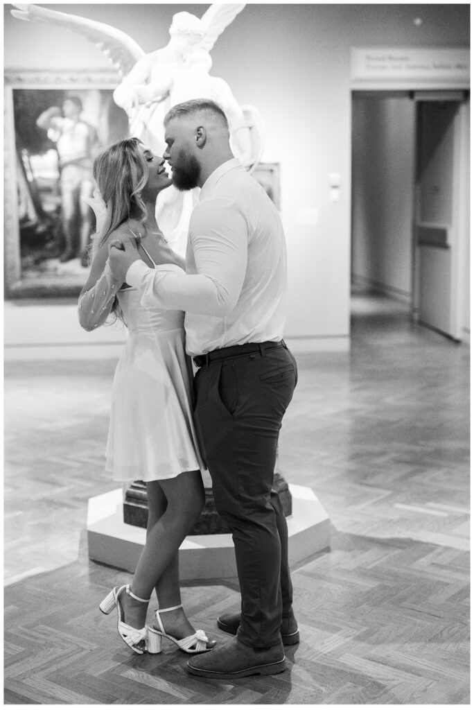 Engaged couple embrace in front of sculpture at the Minneapolis Institute of Art. 