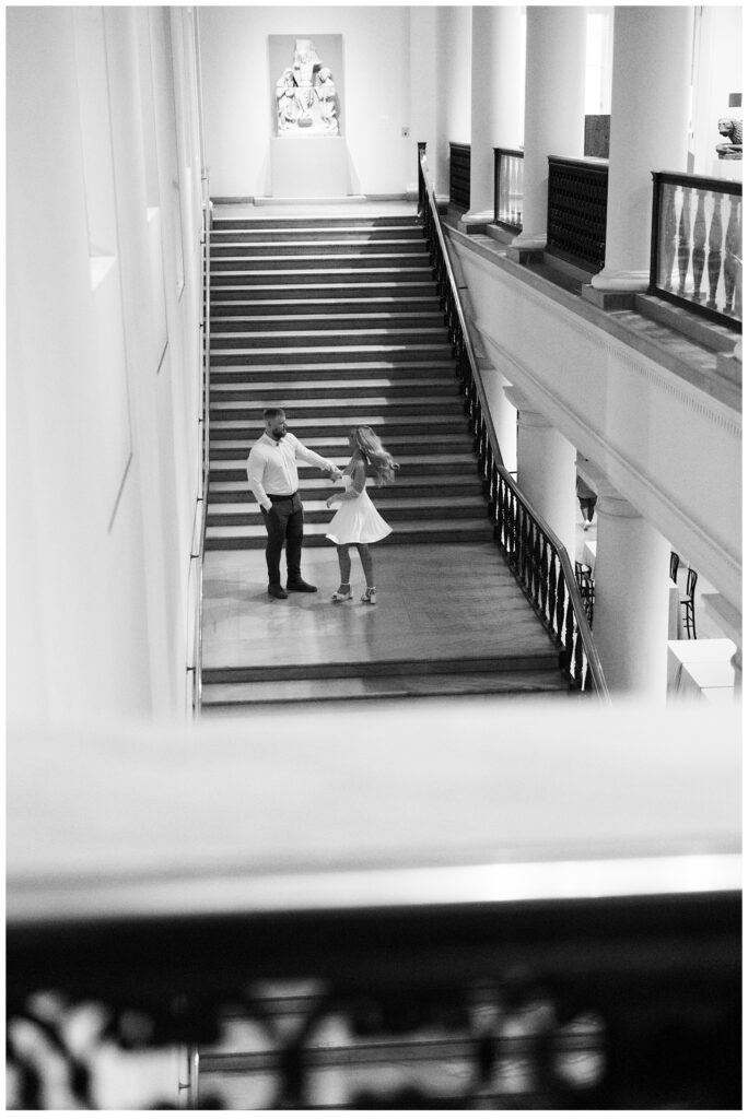 Man twirls fiancée on the steps of art museum for engagement photo session in Minneapolis.  