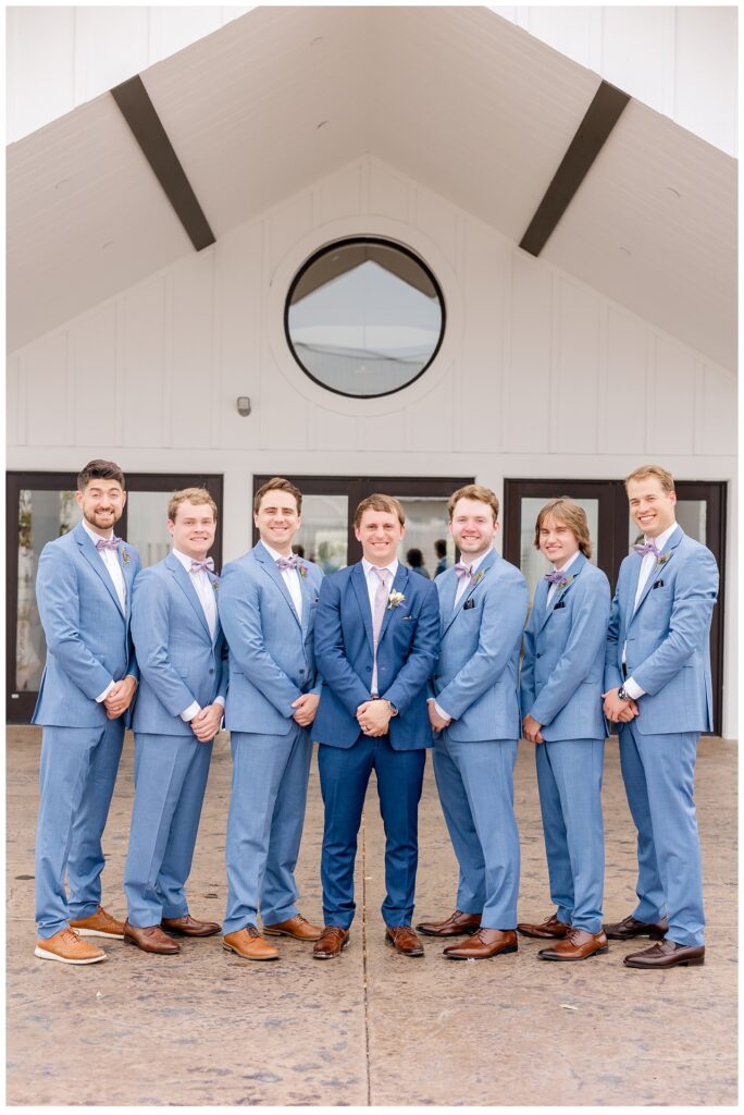 Groom and groomsmen pose with hands clasped in front of them outside of Equestria West. 